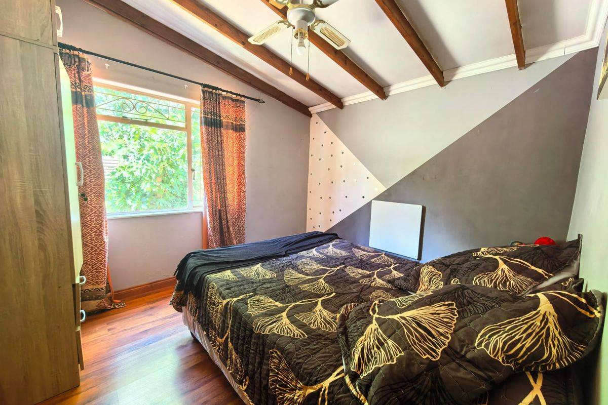 A bedroom featuring exposed timber ceiling beams, a ceiling fan, laminate flooring, and a built-in wardrobe with a wall-mounted heater.
