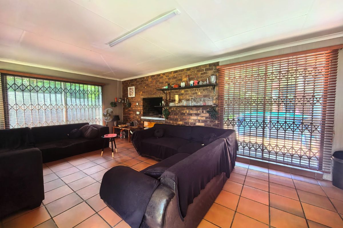Spacious living room featuring an exposed brick wall, terracotta floor tiles, and large windows with security gates, offering a functional and well-lit living space.