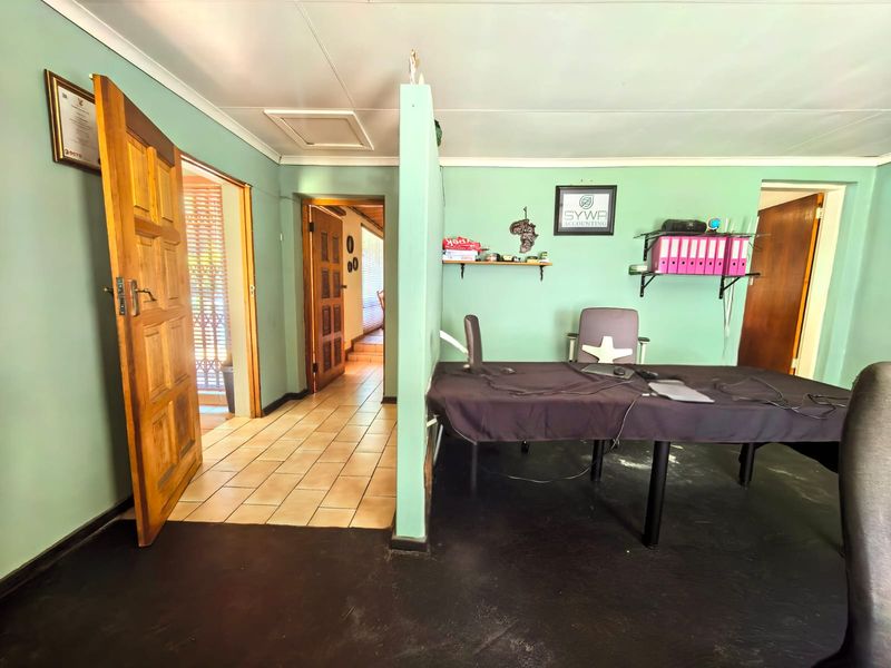 A functional office space featuring a partition wall, tiled flooring, and multiple timber door access points, suitable for a home workspace or study.