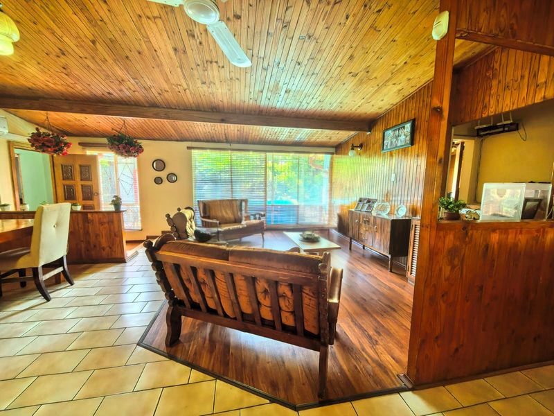 Spacious open-plan living area featuring a combination of tiled and timber flooring, warm timber wall paneling, and a classic timber ceiling with a fan.