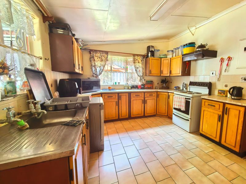 A dated kitchen featuring wooden cabinetry, tiled flooring, and a stainless steel sink, offering significant potential for modernization and renovation.