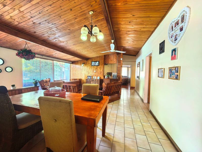 Spacious open-plan living and dining area featuring a distinctive timber-clad vaulted ceiling, exposed beams, and neutral ceramic floor tiles.