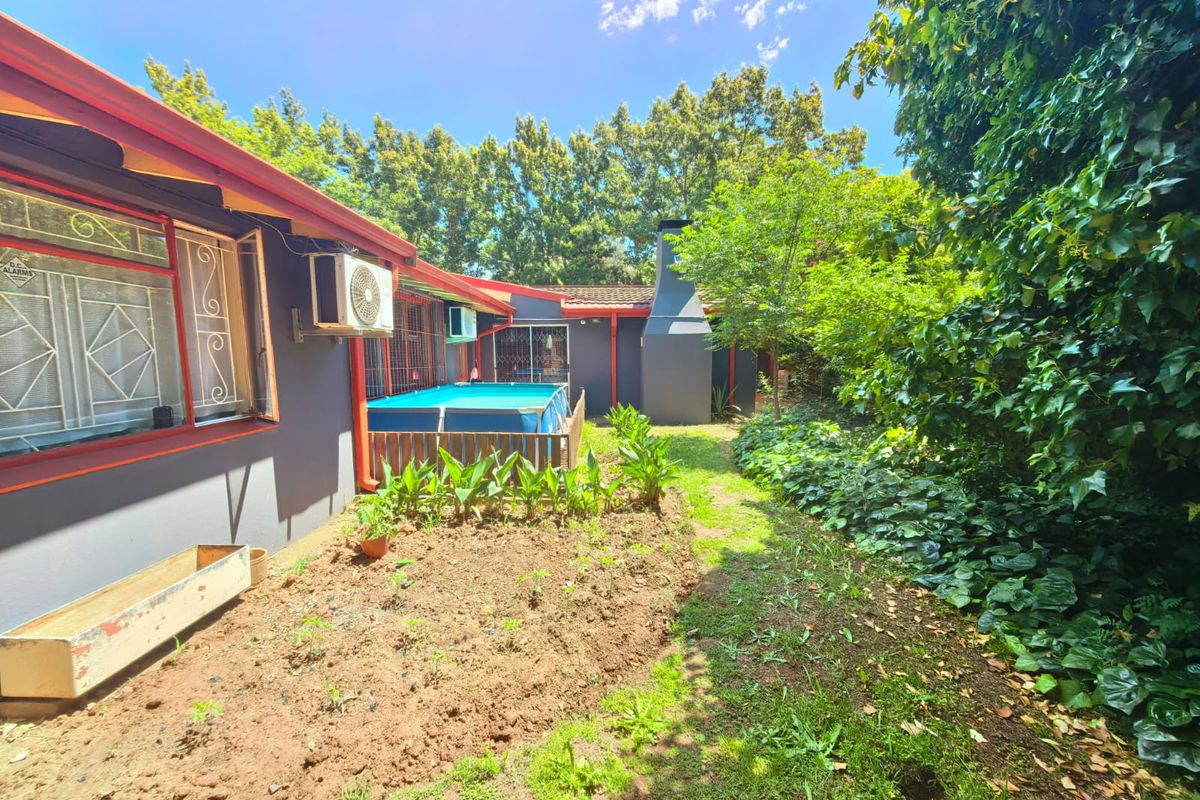 Rear exterior view of the property featuring a garden area, outdoor fireplace, and security-fitted windows along the building facade.