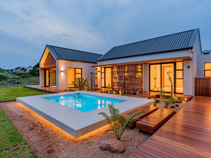 A beautifully landscaped rear exterior featuring a modern swimming pool, extensive timber decking, and contemporary architectural design with warm ambient lighting.