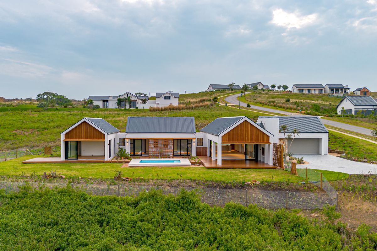 Aerial view of a modern residential property featuring a swimming pool, timber decking, and multiple gabled roof structures set within a landscaped estate.