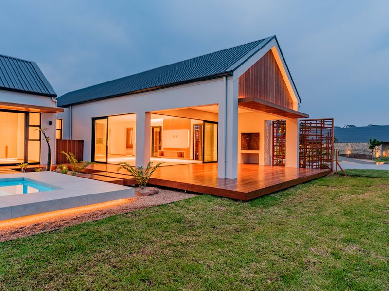 Modern rear exterior featuring a swimming pool, expansive timber decking, built-in braai area, and seamless indoor-outdoor flow through large sliding glass doors.