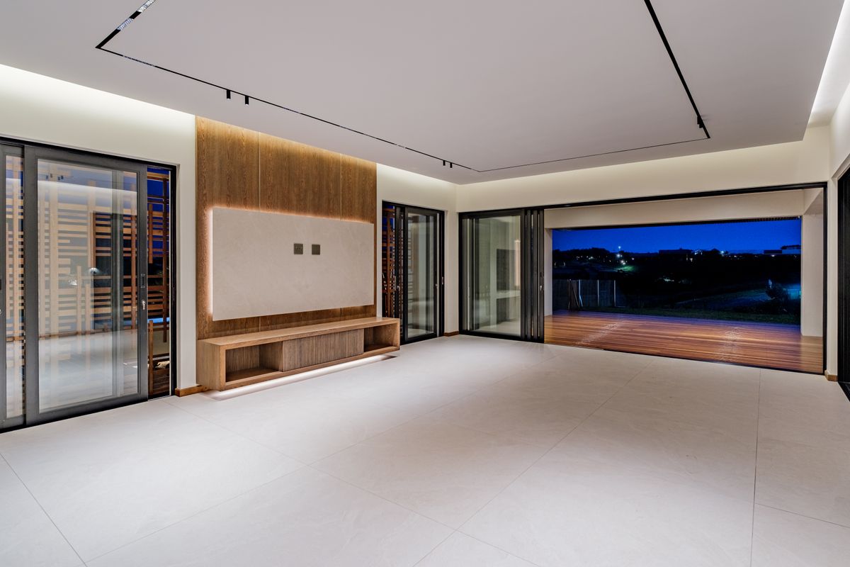 Spacious modern living area featuring large format floor tiles, recessed track lighting, and a custom wood-paneled media wall with integrated lighting.