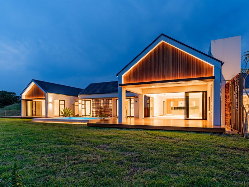 Modern rear elevation featuring timber cladding, expansive sliding glass doors, a swimming pool, and integrated timber decking under a pitched roof design.