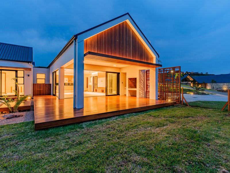 A modern covered patio featuring high-quality timber decking, a built-in braai, and seamless indoor-outdoor flow through large sliding glass doors.