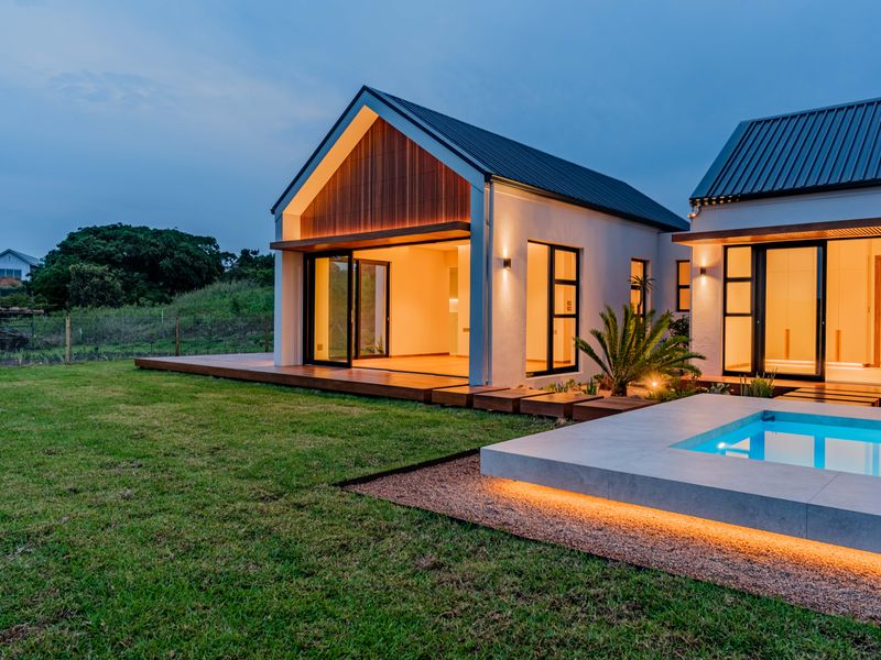 Modern rear exterior featuring a swimming pool, timber decking, and contemporary architectural design with large sliding glass doors opening to the garden.