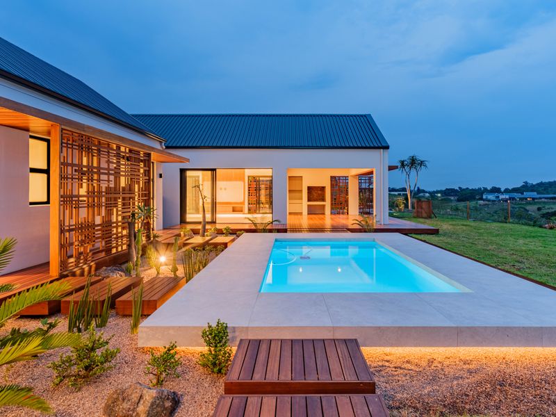 Modern outdoor living area featuring a pristine swimming pool, timber decking, and architectural privacy screens, perfect for evening relaxation and entertainment.