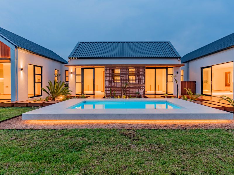 Modern architectural home featuring a central swimming pool, timber decking, and expansive sliding glass doors opening to the landscaped garden.