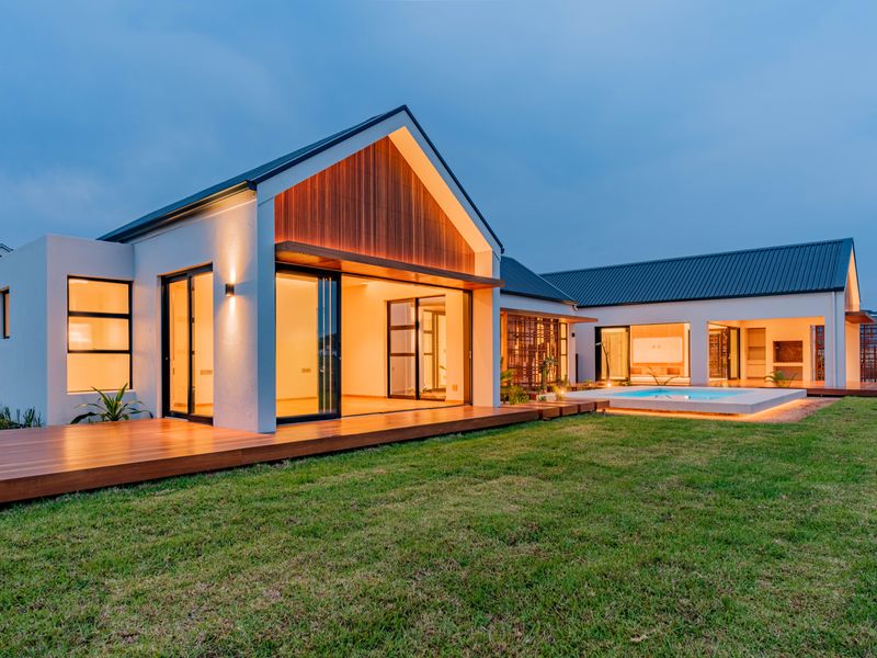 Modern rear elevation featuring a swimming pool, expansive timber decking, and large sliding glass doors connecting the interior to the landscaped garden.