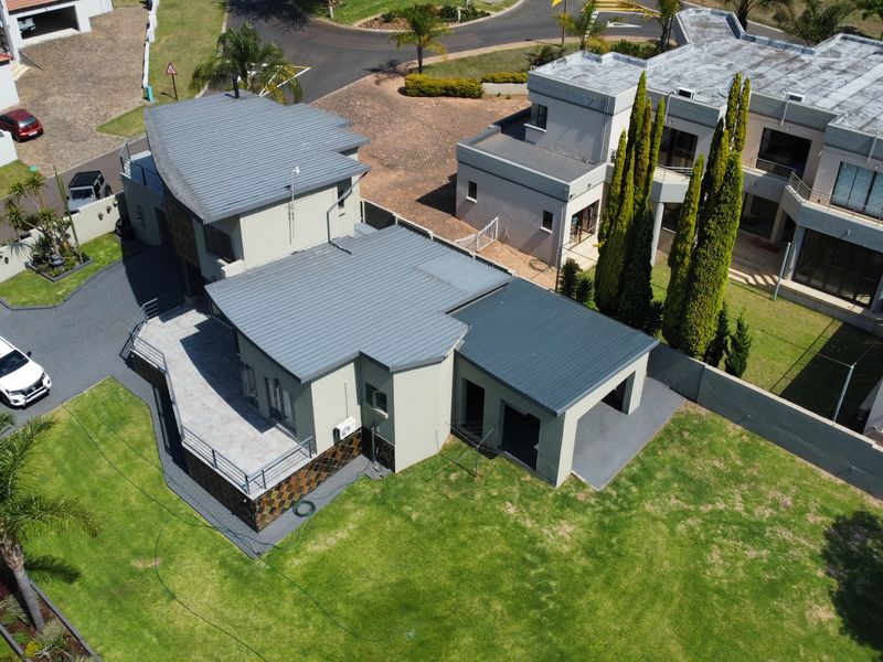 Aerial view of the property showcasing the modern metal roof, paved driveway, private lawn, and attached garage within a residential estate setting.