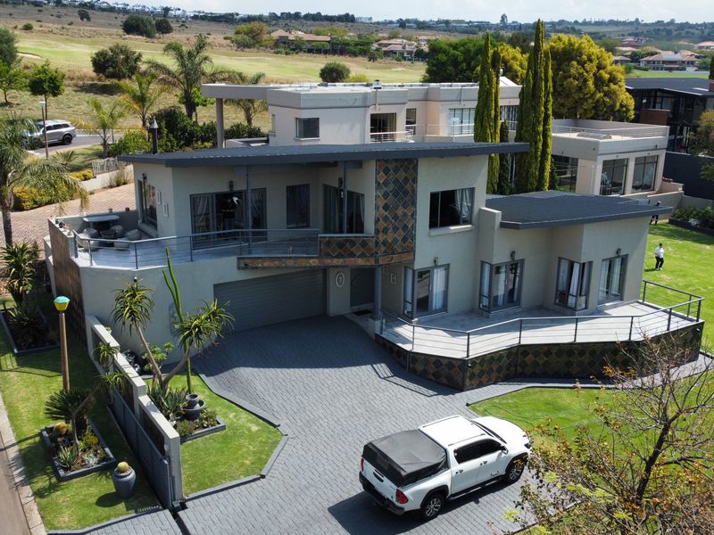Aerial view of a modern multi-level residential property featuring a paved driveway, landscaped garden, and elevated balcony areas.