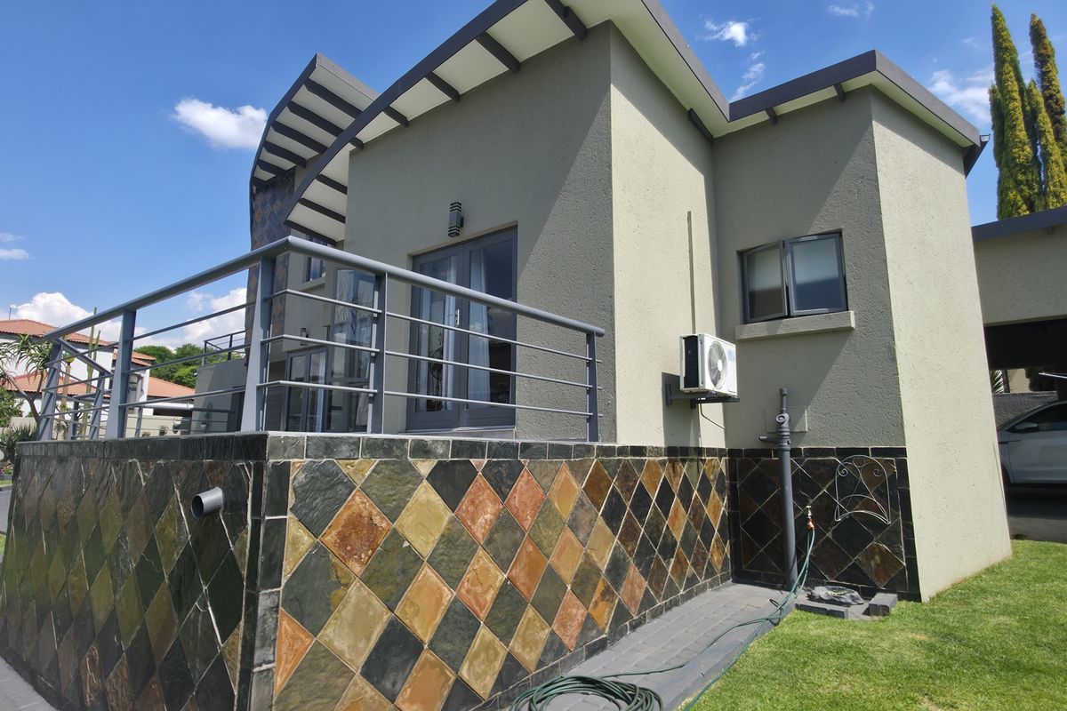 Rear view of the property featuring a raised patio with metal balustrade, slate tile cladding, and a well-maintained lawn area.