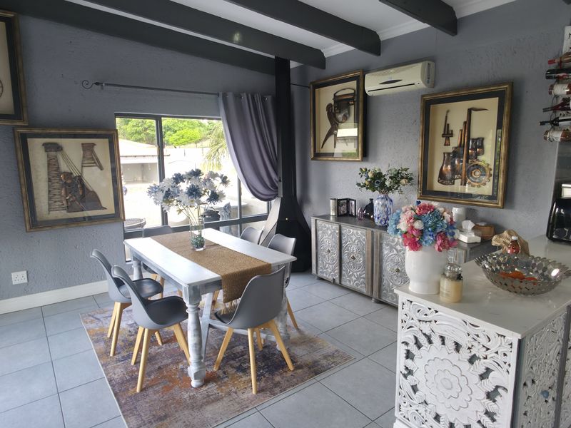 Open-plan living and dining area featuring exposed ceiling beams, a fireplace, split-system air conditioning, and a modern kitchen with stone countertops.