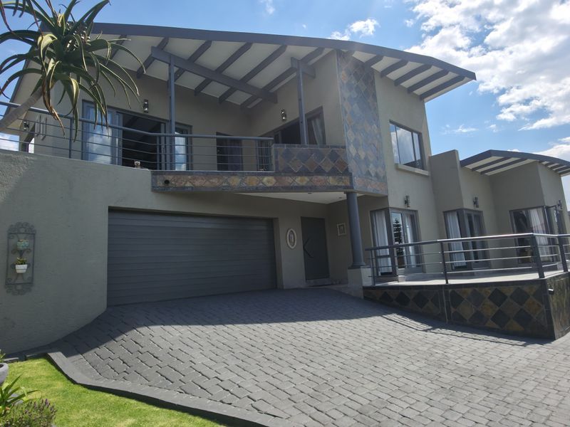 Front elevation of a modern multi-level house featuring a paved driveway, double garage, and an upper-level balcony with metal railings.