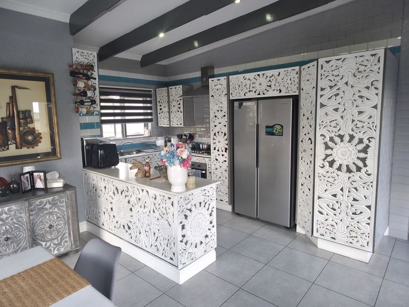 A kitchen featuring decorative carved cabinetry, a central island, tiled flooring, and exposed ceiling beams, offering a unique aesthetic with integrated appliances.