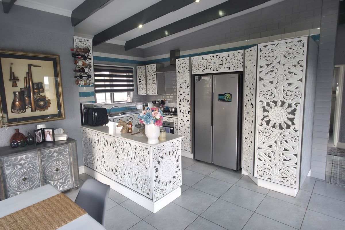 A kitchen featuring decorative carved cabinetry, a central island, tiled flooring, and exposed ceiling beams, offering a unique aesthetic with integrated appliances.