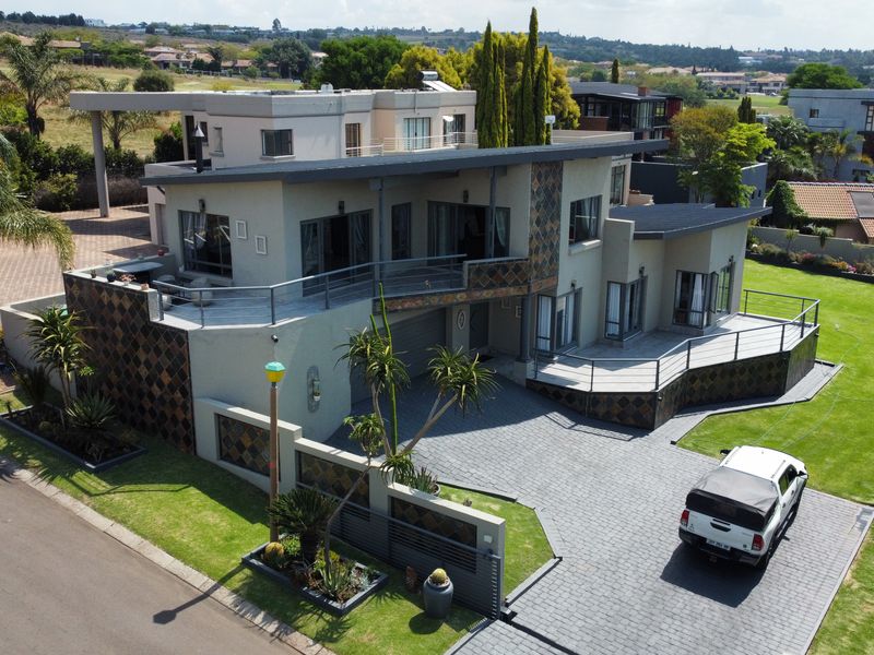 Aerial view of a modern multi-level residential property featuring a paved driveway, expansive balconies, and well-maintained landscaped gardens.