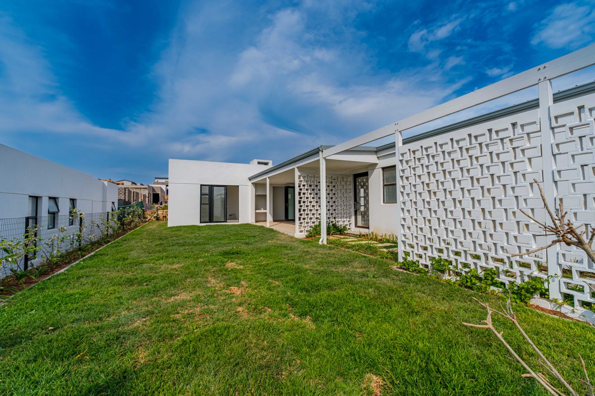 Rear view of a modern house featuring a covered patio, decorative breeze block wall, and a well-maintained lawn.