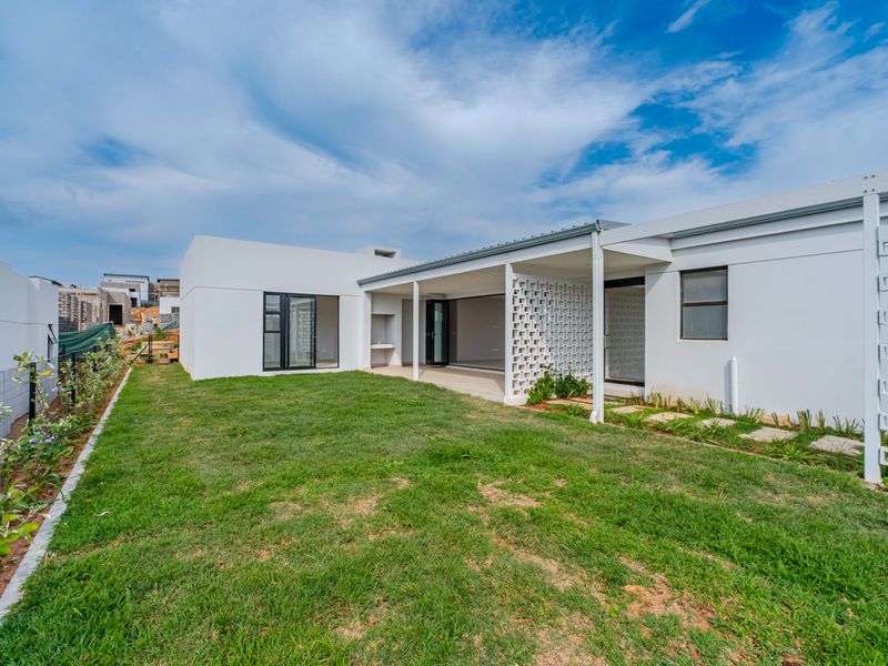 A modern rear exterior view featuring a covered patio with a built-in braai, decorative breeze block wall, and a well-maintained lawn.