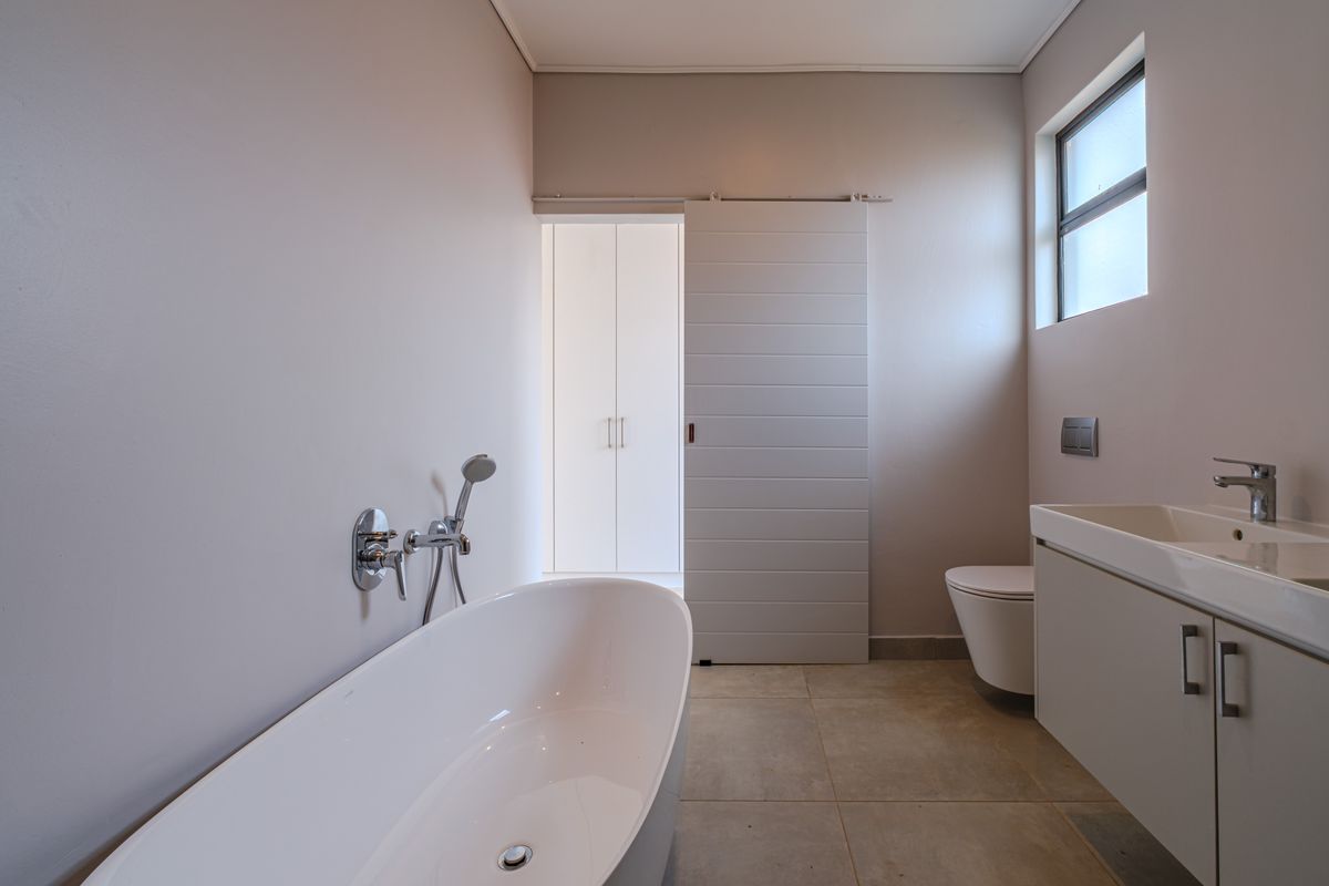 Modern bathroom featuring a sleek freestanding bathtub, wall-mounted shower fixtures, a contemporary vanity, and a wall-hung toilet with neutral tiled flooring.