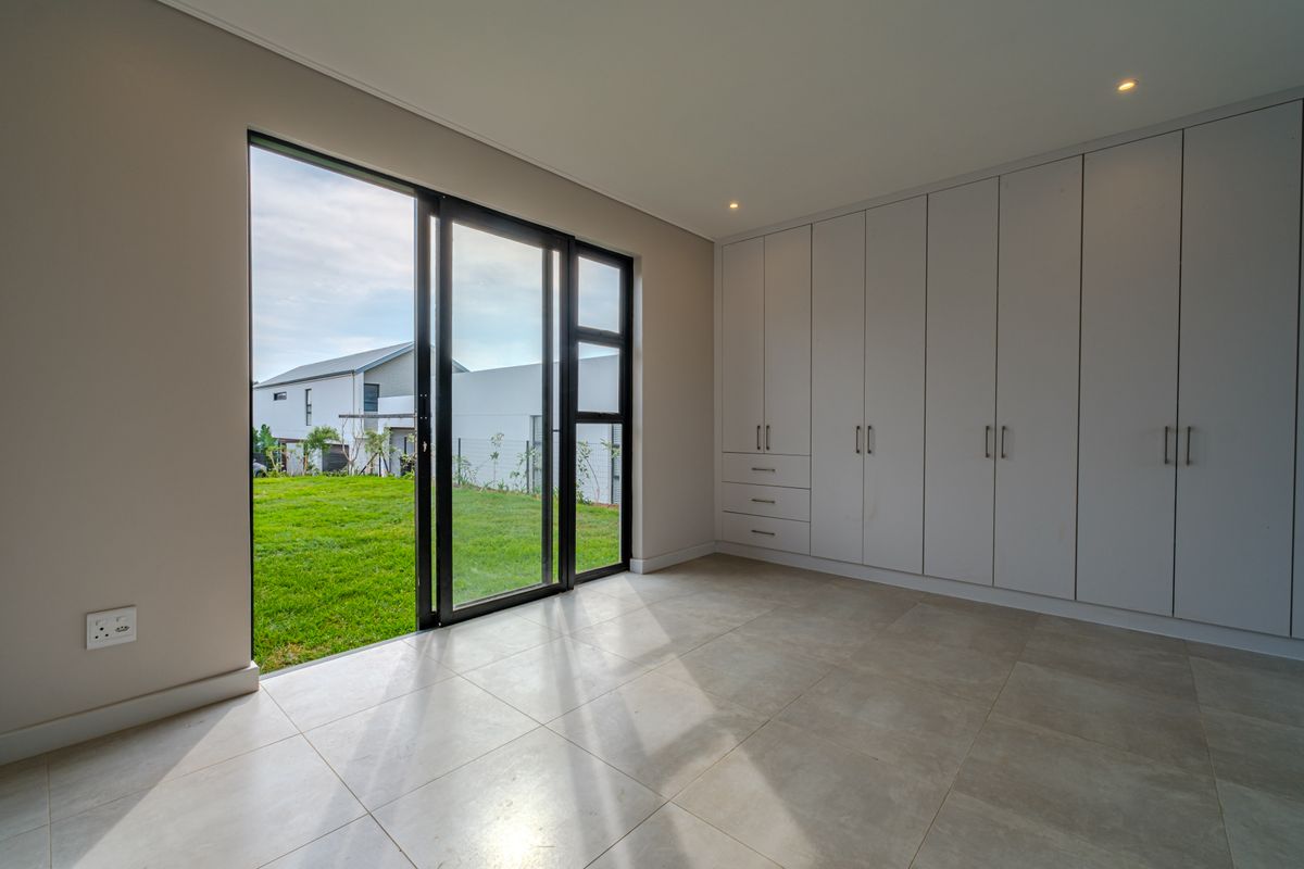 A bright, modern bedroom featuring neutral tiled flooring, extensive built-in cabinetry, and large sliding glass doors providing direct access to the garden.