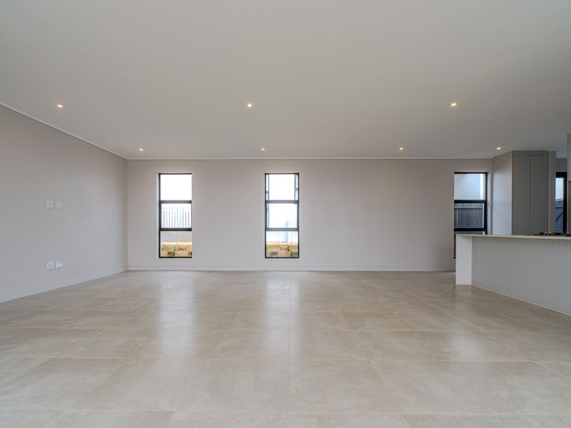 Spacious open-plan living area featuring neutral tiled flooring, recessed downlights, and a modern kitchen island with integrated hob, offering a bright and versatile layout.