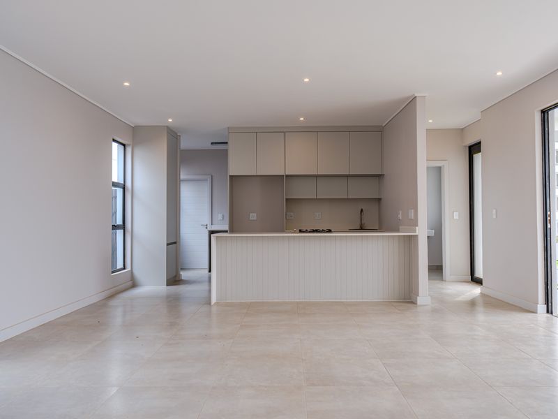 A bright and modern open-plan living and kitchen area featuring neutral cabinetry, a central island with a hob, and large sliding doors leading outdoors.