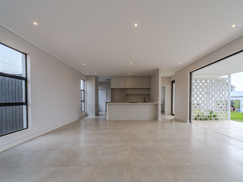 Spacious open-plan living and kitchen area featuring modern tiled floors, recessed lighting, and seamless flow to an outdoor patio through large sliding glass doors.
