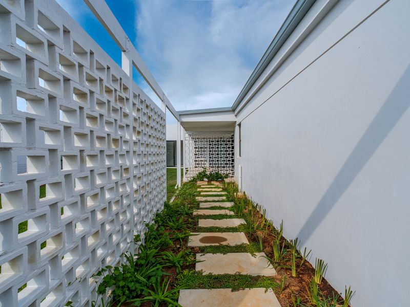 A well-maintained side walkway featuring a decorative breeze block screen wall and a stone paver path set within a landscaped garden area.