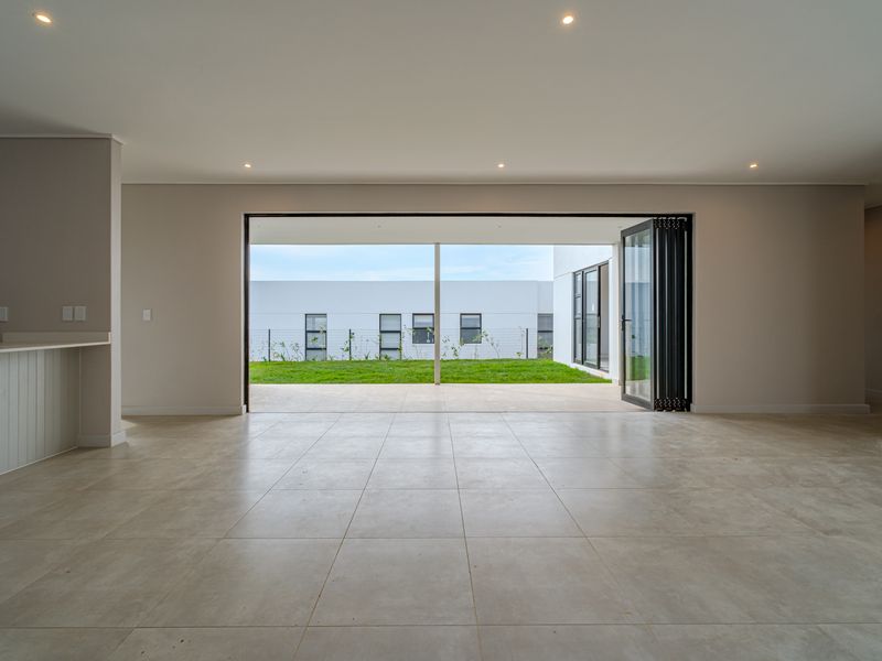 Spacious open-plan living area featuring large bi-fold doors that open onto a covered patio and garden, finished with modern neutral tiles and recessed lighting.