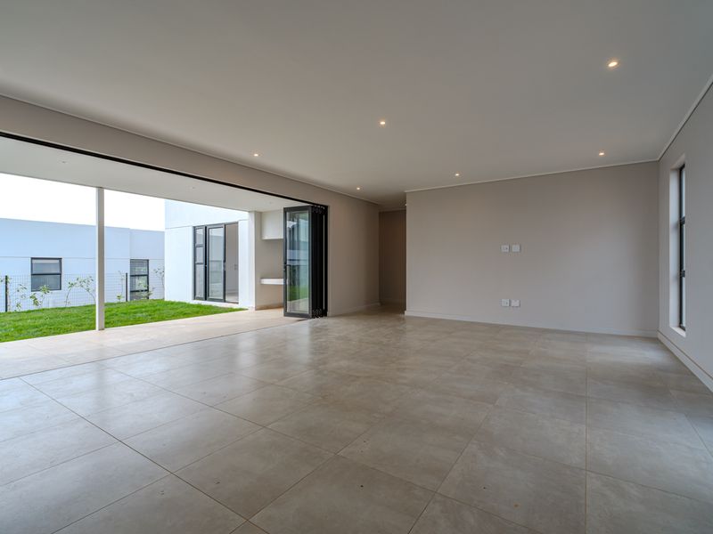 Spacious, modern open-plan living area featuring large bi-fold doors that open onto a covered patio and garden, finished with neutral floor tiles.
