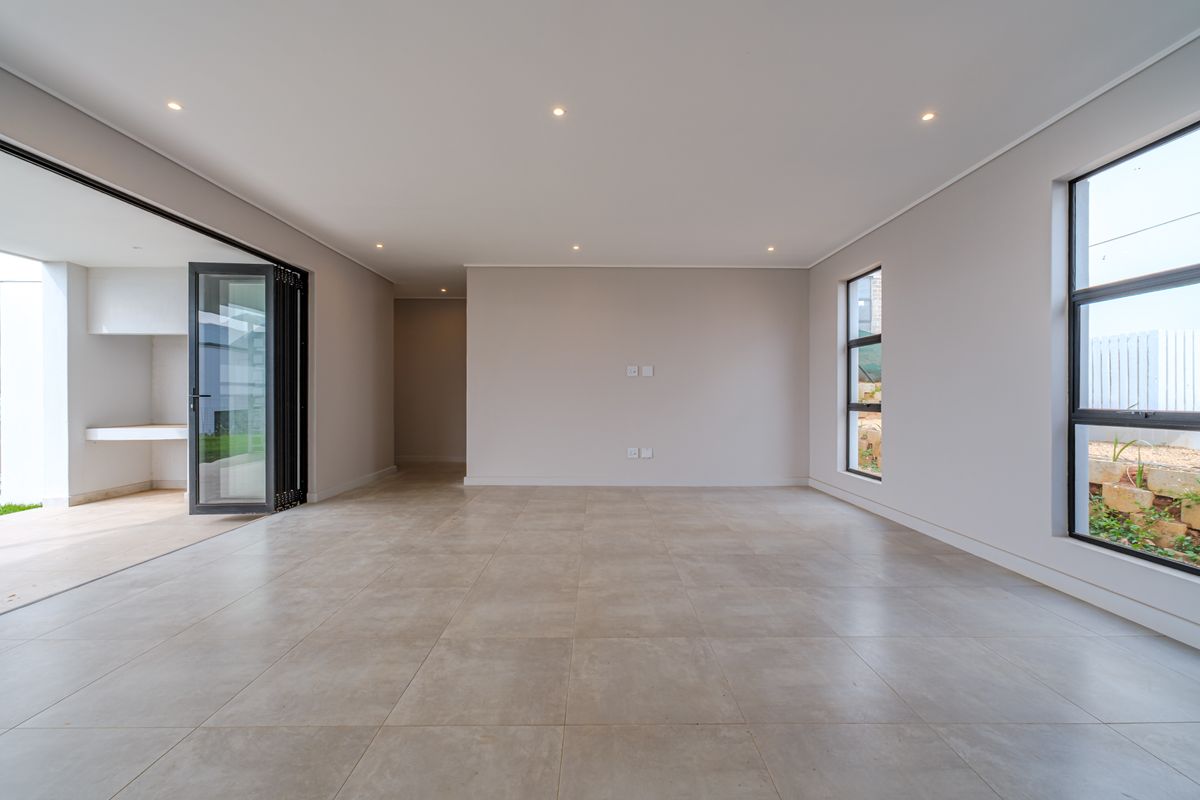 Spacious, modern open-plan living area featuring large format floor tiles, recessed lighting, and seamless access to an outdoor patio through aluminium stacker doors.