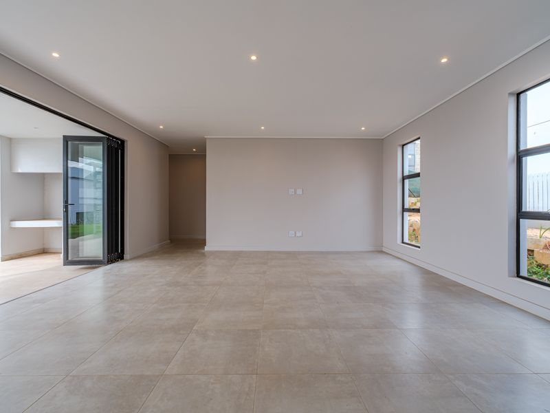 Spacious, modern open-plan living area featuring large format floor tiles, recessed lighting, and seamless access to an outdoor patio through aluminium stacker doors.