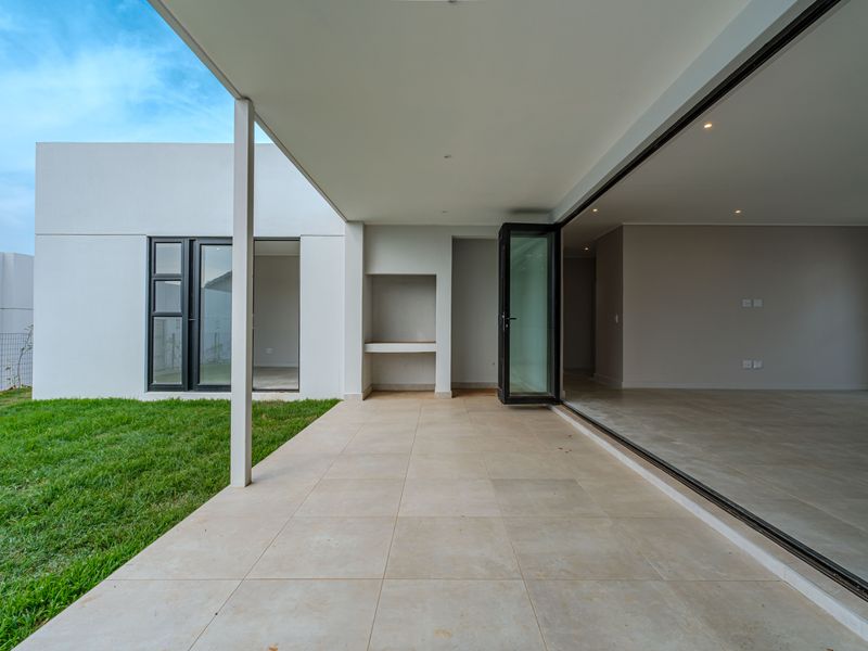 A modern covered patio featuring tiled flooring, a built-in braai, and seamless stacking glass doors that open into the interior living space.