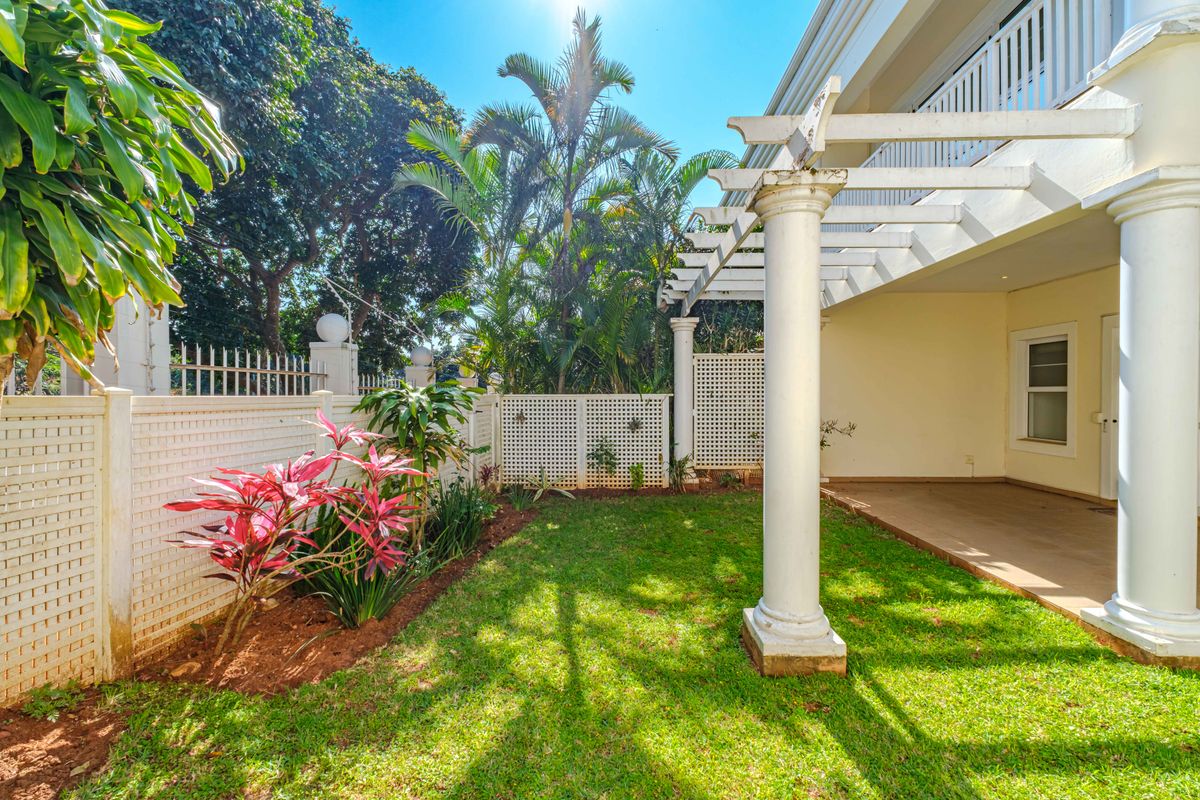 A well-maintained rear garden featuring a paved patio area with a pergola supported by classical columns, enclosed by white lattice fencing.