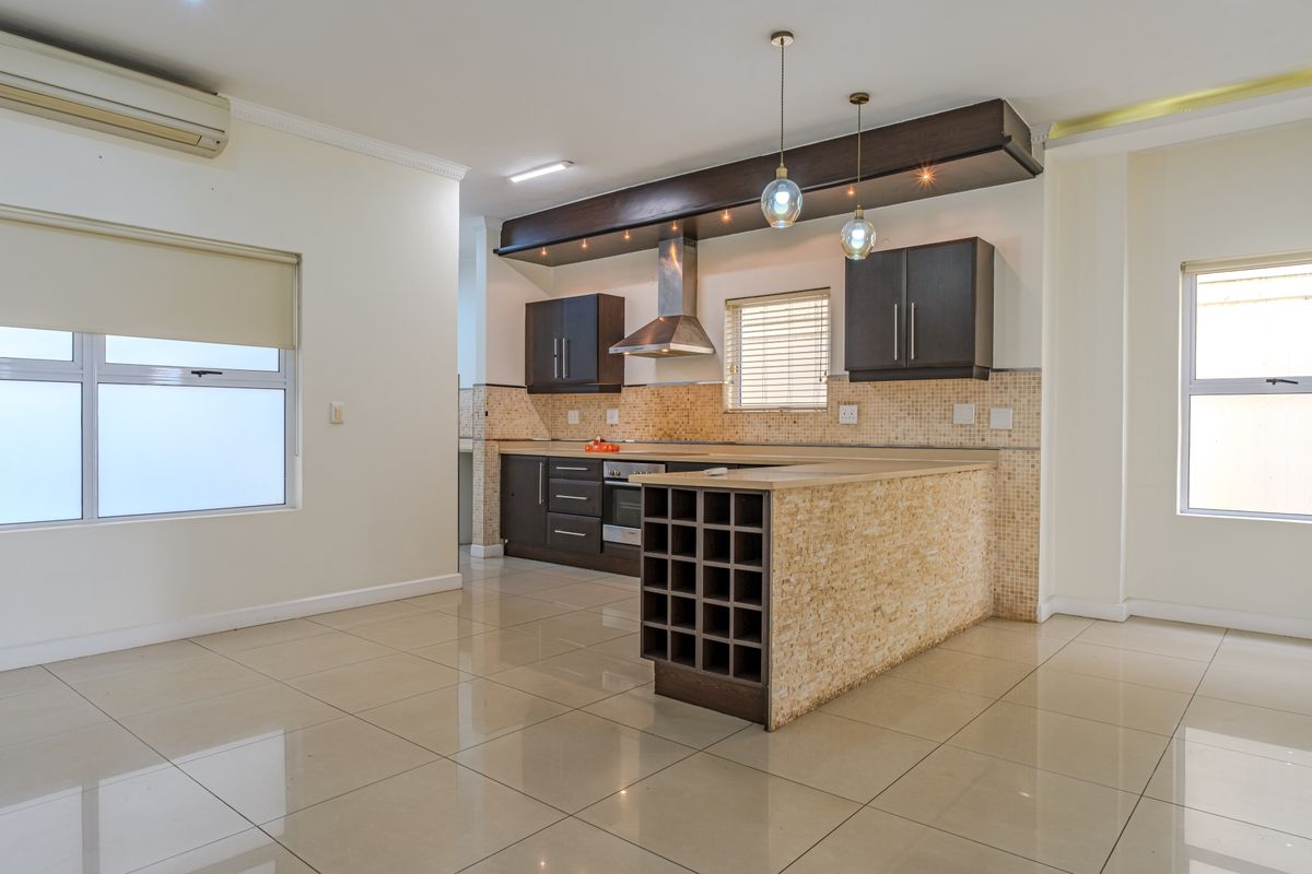 Modern open-plan kitchen featuring dark wood cabinetry, stone countertops, mosaic tile backsplash, built-in oven, extractor fan, and a convenient breakfast bar with wine storage.