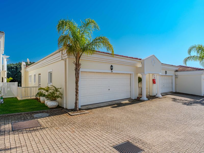 A well-maintained front exterior view of a residential property featuring a double garage, paved driveway, and classic architectural columns.