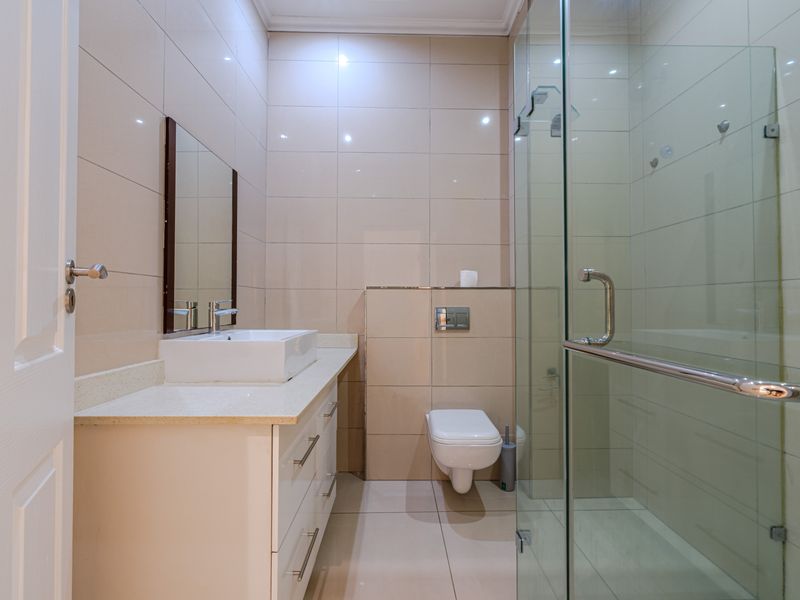 A modern, clean bathroom featuring a wall-mounted toilet, a glass-enclosed shower, and a vanity with a countertop basin.
