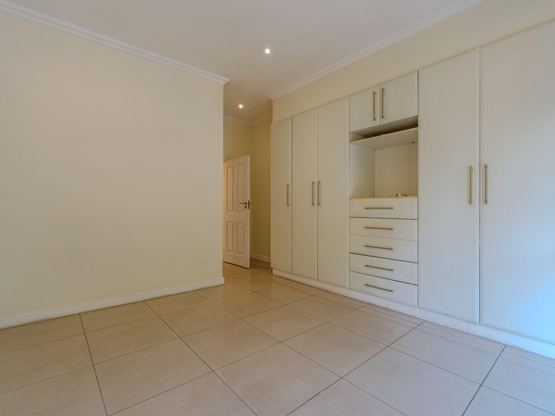 A bright, empty bedroom featuring neutral tiled flooring, recessed lighting, and extensive built-in cabinetry with integrated drawers.