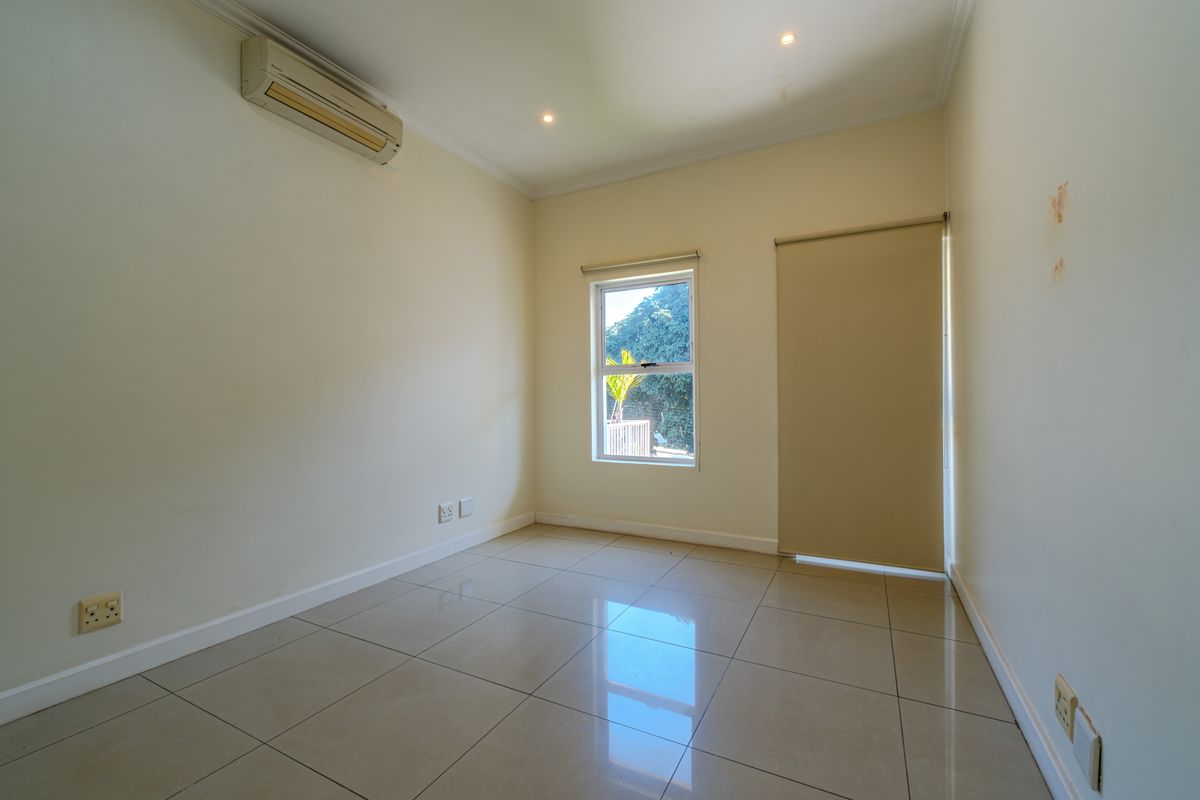 A bright, empty bedroom featuring tiled flooring, recessed downlighting, a wall-mounted air conditioning unit, and neutral wall finishes.