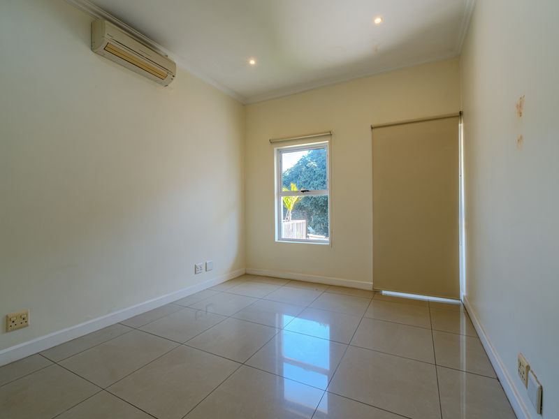 A bright, empty bedroom featuring tiled flooring, recessed downlighting, a wall-mounted air conditioning unit, and neutral wall finishes.
