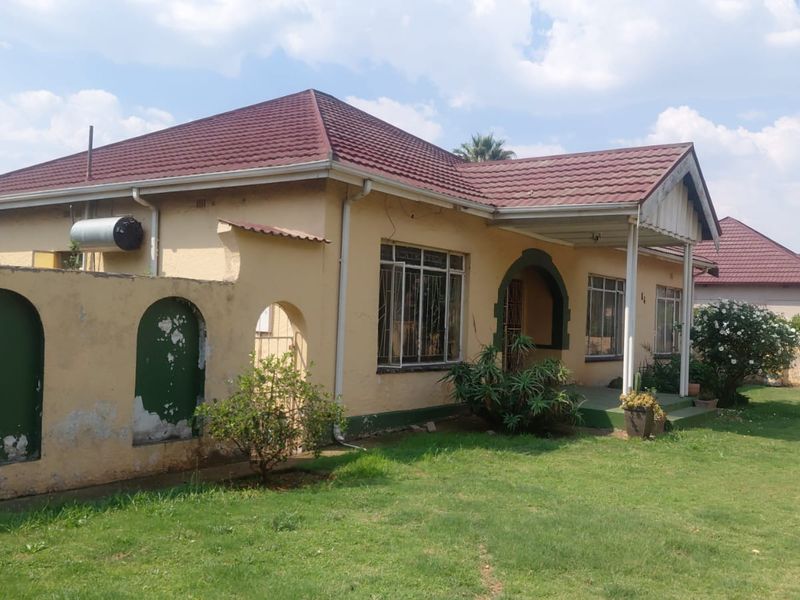 Front view of a single-story house featuring a tiled roof, covered porch, and a surrounding boundary wall with a lawn area.