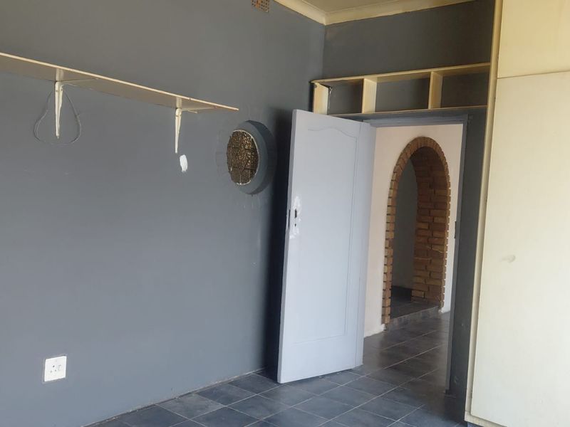 An empty bedroom featuring built-in cupboards, a unique porthole window, and an arched doorway leading to an adjacent space.