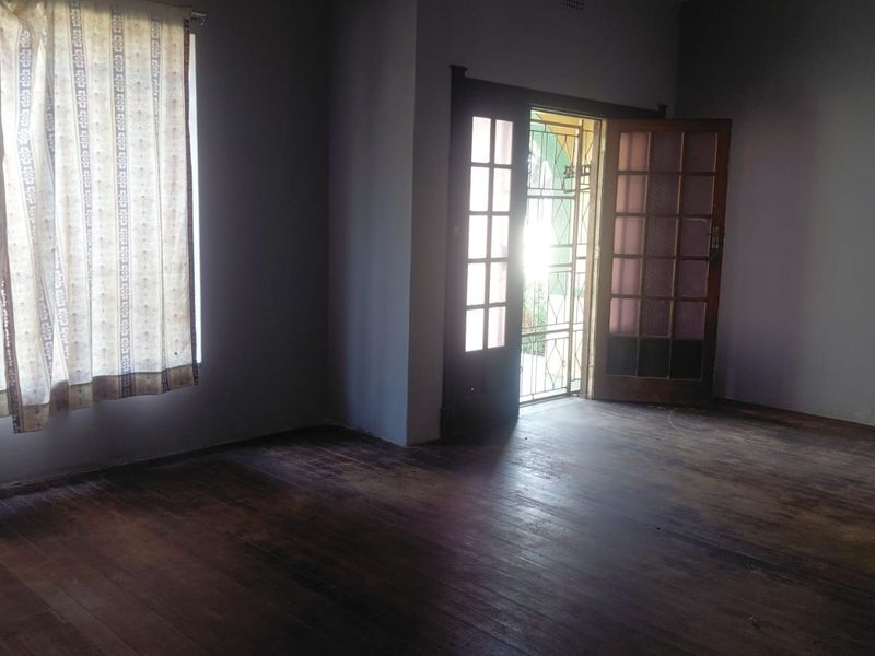 An empty living room featuring original timber flooring and classic french doors leading to an exterior entrance.