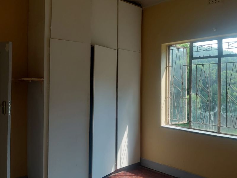 A vacant bedroom featuring built-in cupboards, timber flooring, and security bars on the window, offering a blank canvas for renovation.