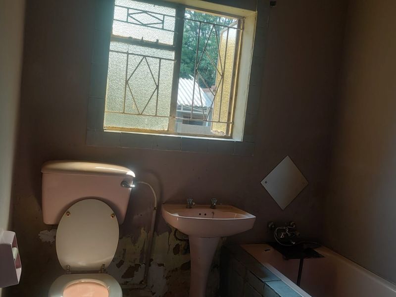 A dated bathroom featuring a vintage pink suite, including a pedestal basin, toilet, and bathtub, requiring significant renovation and cosmetic updates.